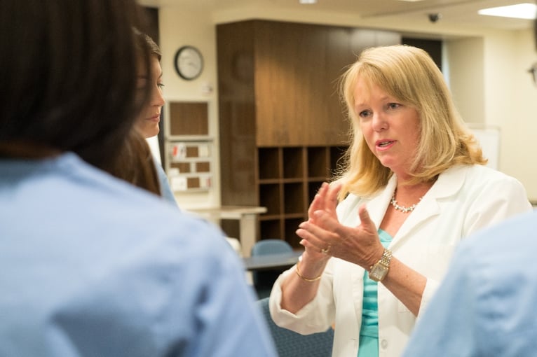 A female nurse and USD faculty member explains a concept to nursing students.